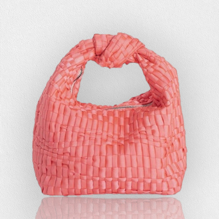 The MARIA LA ROSA MINI KNOT HANDLE BAG is handmade in Italy from coral pink woven ribbon fabric, features a knotted handle and zippered opening, and is shown on a light textured background with a subtle reflection.