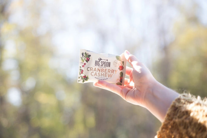 A BIG SPOON ROASTERS - CRANBERRY CASHEW SNACK BAR, by BIG SPOON ROASTERS, with cranberry and cashew illustrations on a cream background. This non-GMO bar is dairy free, gluten free, soy free, and palm oil free for a wholesome snack.