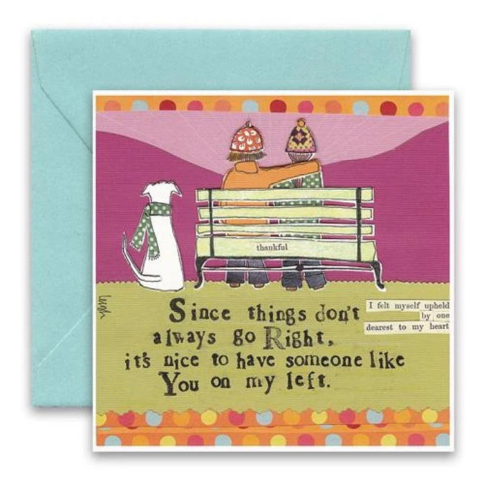 Illustration of a person and a cat sitting on a bench, both wearing colorful hats in vibrant collage art style, with a background awash in pink and orange hues over a green field. Featured on the Curly Girl Designs - Anything With Sprinkles Card by Curly Girl Design, Inc., the text reads, "Since things don't always go right, it's nice to have someone like you on my left.