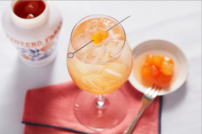Three small, round desserts topped with orange garnish and chopped pistachios sit on a white plate, drizzled with FABBRI - CANDIED GINGER IN SYRUP by GOURMET FOOD SOLUTIONS. Crumbled toppings surround them; a jar rests blurred in the background.