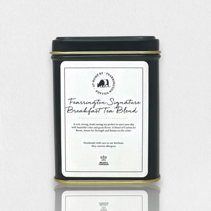 A black metal tin labeled “FEARRINGTON SIGNATURE COLLECTION - FEARRINGTON SIGNATURE BREAKFAST TEA TIN” by FEARRINGTON HOUSE sits on a light surface, featuring a goat logo and containing premium loose leaf tea crafted by Harney and Sons.