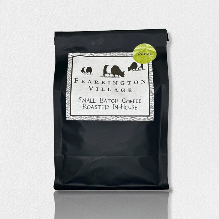 A black bag of BELTED GOAT FEARRINGTON SIGNATURE COLLECTION - SMALL BATCH HOUSE BLENDED DECAF COFFEE BEANS, featuring a green "DECAF" sticker and crafted from Brazilian and Colombian beans, is shown against a white background.
