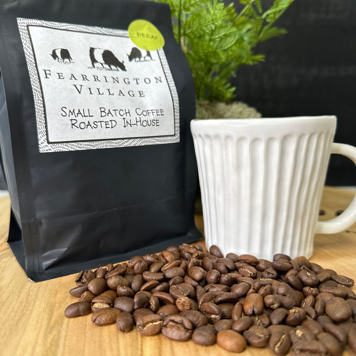 A black bag of BELTED GOAT FEARRINGTON SIGNATURE COLLECTION - SMALL BATCH HOUSE BLENDED DECAF COFFEE BEANS, featuring a green "DECAF" sticker and crafted from Brazilian and Colombian beans, is shown against a white background.