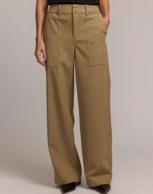 A person is standing against a neutral background with one hand in their pocket, wearing the HINSON WU KELLY Traveler’s Twill Pant in khaki—featuring a high-waisted, wide-leg silhouette, front patch pockets, and a double button closure.