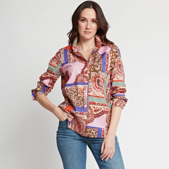 A woman stands against a plain background wearing the HINSON WU - REESE LONG SLEEVE SHIRT, a relaxed fit patchwork paisley top in pink, red, purple, and green, paired with blue jeans. She looks confidently at the camera with one hand in her pocket.