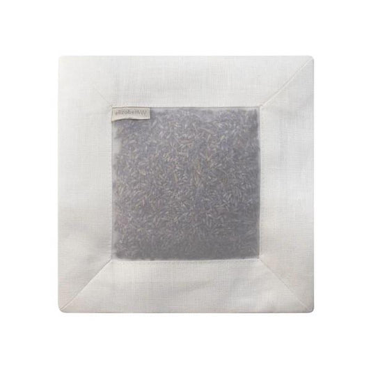The E WIGHTMAN & CO LAVENDER SQUARE SACHET IVORY LINEN is an elegant white linen sachet with a clear window showcasing dried lavender buds and a small tag, perfect for adding a refined scent to your closet.