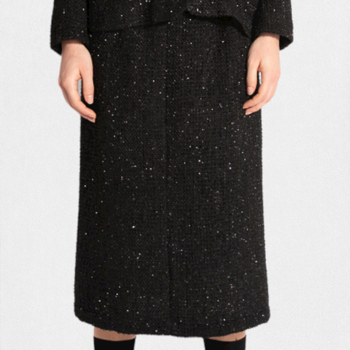 A woman wears the MEIMEIJ LUREX TWEED SKIRT with a black textured ruffle blazer, a white tee with black text, and black shoes with matching socks, posed against a white background.