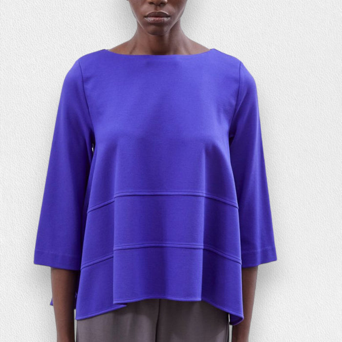 A person wears the MEIMEIJ Oversized Crew Neck Top in bright blue, featuring horizontal seam details, paired with gray pants, standing against a light textured background.