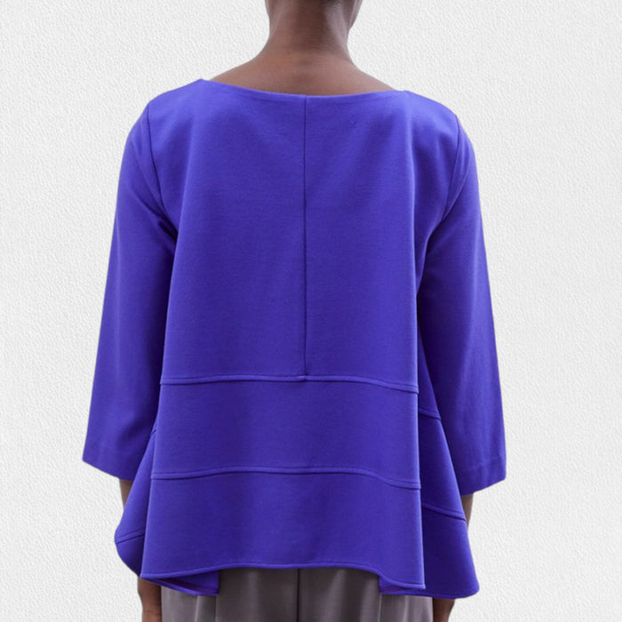 A person wears the MEIMEIJ Oversized Crew Neck Top in bright blue, featuring horizontal seam details, paired with gray pants, standing against a light textured background.