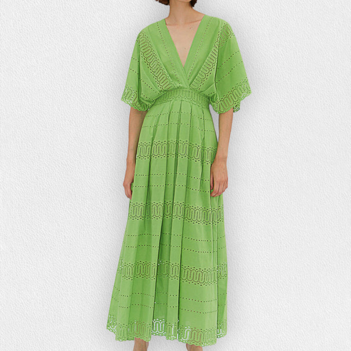 A person wears the MILVA SANGALLO DRESS, a light green cotton v-neck with eyelet details, short wide sleeves, and an ankle-length hem, standing against a plain white textured background.