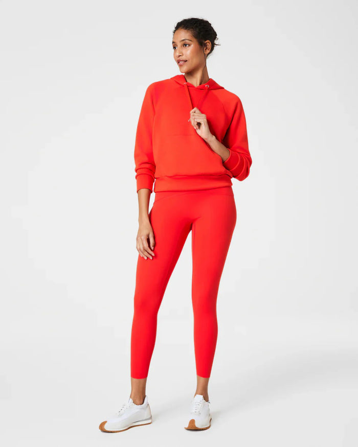 A person wears SPANX - BOOTY BOOST 7/8 LEGGINGS in high-waisted royal blue performance fabric with black athletic shoes, standing hand on hip against a plain white background. Only their lower body is visible; upper body and face are not shown.
