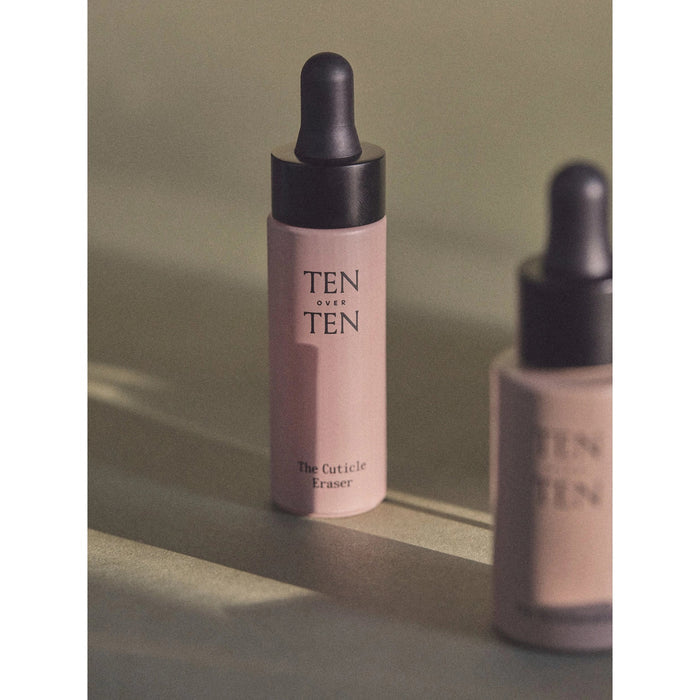 A dropper bottle of TENOVERTEN - CUTICLE ERASER by TEN OVER TEN is bathed in soft, diffused light, creating a calm manicure vibe. A second blurred bottle appears in the foreground, with muted neutral tones accenting this gentle cuticle remover.