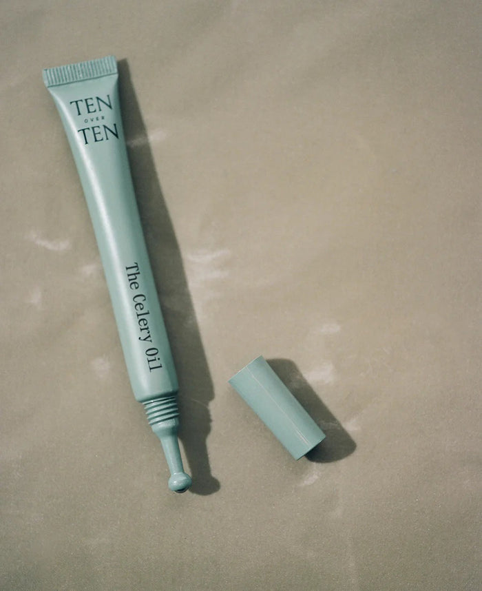 A light blue tube labeled "TENOVERTEN - THE CELERY OIL" by TEN OVER TEN, known for its nourishing nail treatment and repair benefits, rests uncapped on a beige surface.