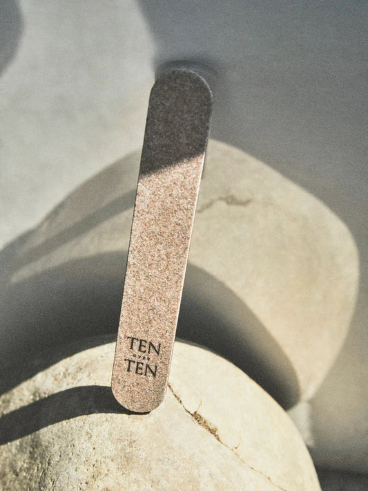The TENOVERTEN - THE ECO NAIL FILE by TEN OVER TEN, printed with "TEN TEN," rests against light stones in soft natural light, ideal for gently shaping natural nails.