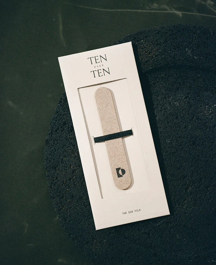 The TENOVERTEN - THE ECO NAIL FILE by TEN OVER TEN, printed with "TEN TEN," rests against light stones in soft natural light, ideal for gently shaping natural nails.