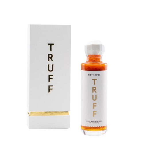 A bottle of TRUFF HOT SAUCE WHITE TRUFFLE with a white and gold label stands beside its matching box, both displaying the TRUFF HOT SAUCE brand. This limited edition features premium white truffle hot sauce.