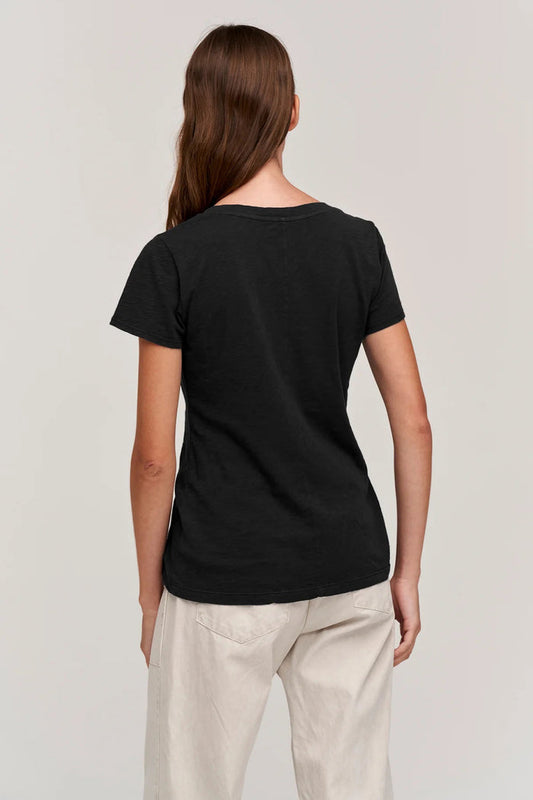 A person with long brown hair is seen from behind, wearing the VELVET BY GRAHAM & SPENCER LILITH V NECK SLUB COTTON TEE in black and light-colored pants, standing against a plain background.