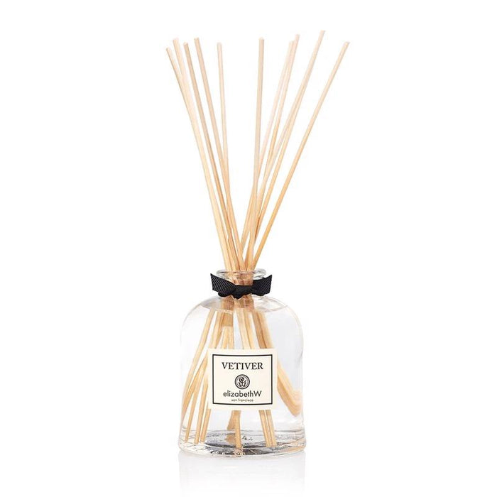 The VETIVER DIFFUSER by E WIGHTMAN & CO features a glass bottle with clear liquid and wooden reeds, topped with a black ribbon. This elegant low-VOC diffuser brings refined vetiver fragrance to your home.
